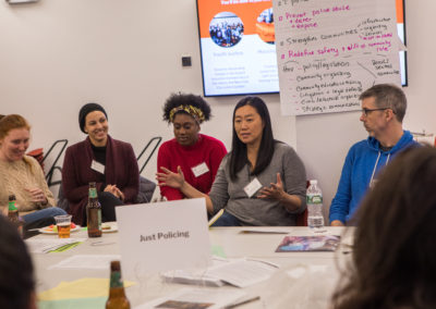 Group of people sitting at a table with a placard on it that says "Just Policing"