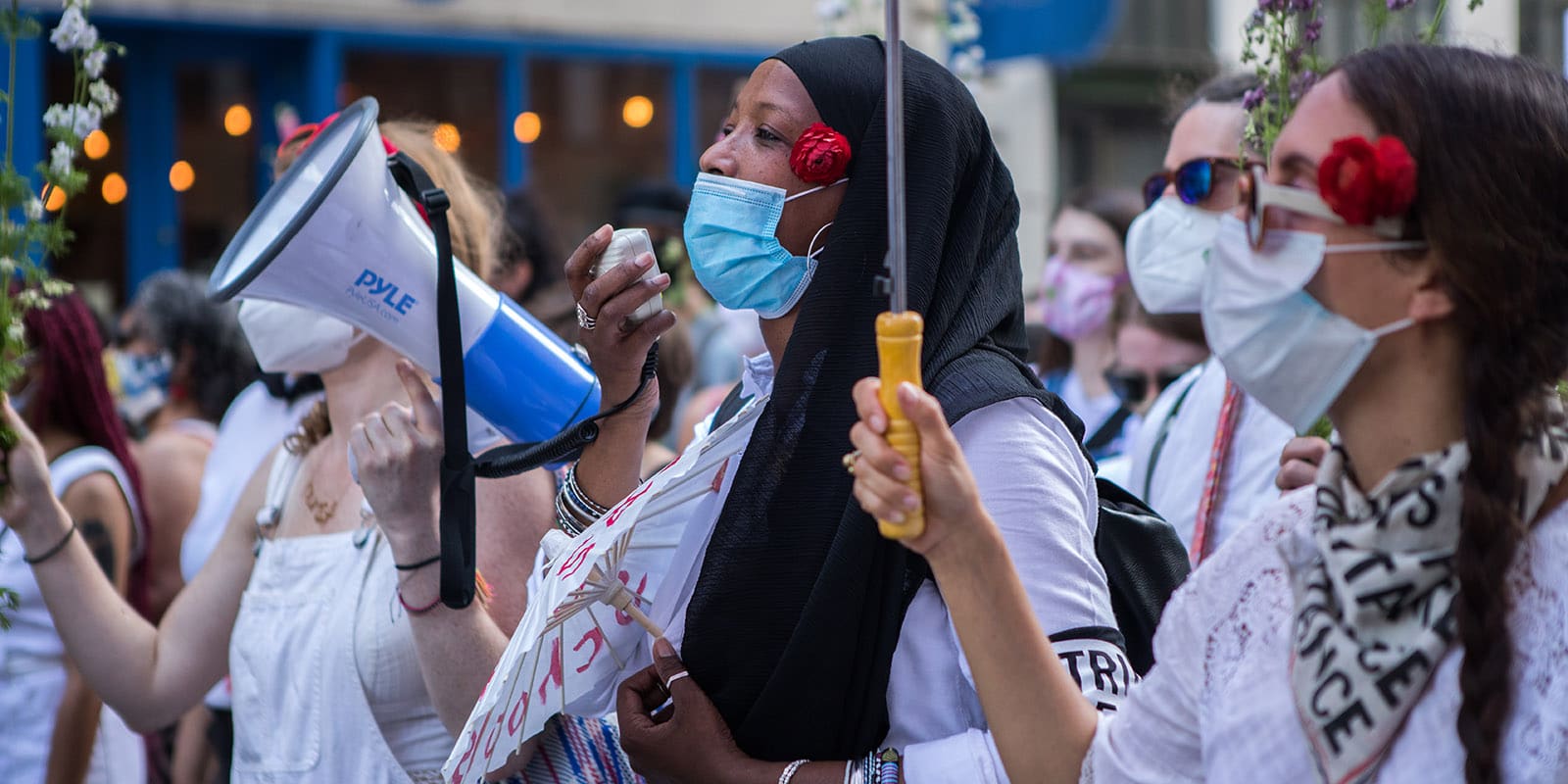 Outdoor protesters with masks and a banner that reads "Fast to Fund Excluded Workers"
