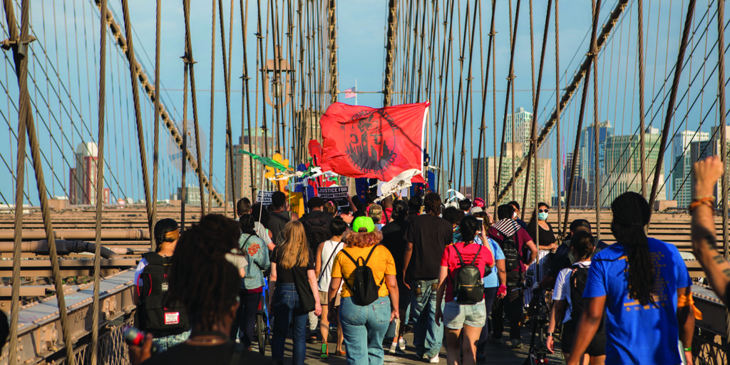 Protesters marching on the Brooklyn Bridge with a banner for Justice Committee