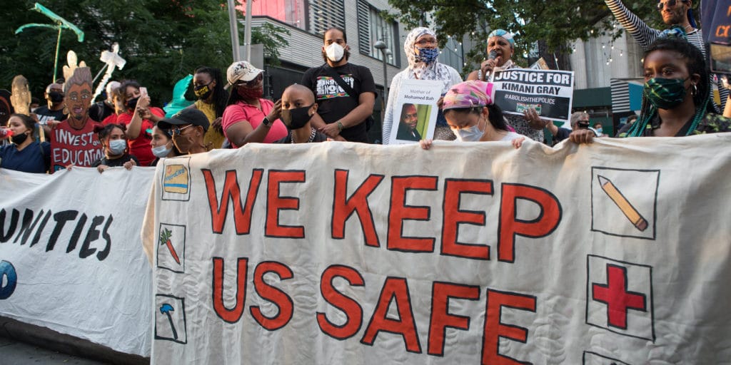 Outdoor protesters with masks and a banner that reads "Fast to Fund Excluded Workers"